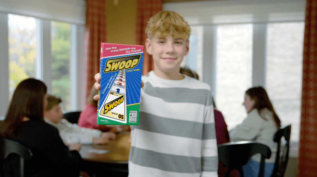 Son holding SWOOP Box with family having fun playing SWOOP in the background